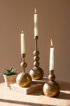 Three decorative candle holders with candles on a wooden surface against a beige background