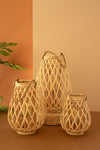 Three natural woven rattan lanterns in different sizes, arranged on a brown surface against a split orange and beige background.