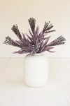 Purple artificial plants in a white vase on a light background