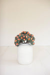 Decorative wreath with orange berries on a white vase against a white background