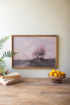 Framed landscape painting on a wall above a wooden table with a bowl of lemons and books.