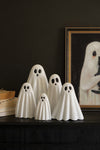 Set of white ghost-shaped decorative items on a dark surface with a framed picture in the background.
