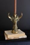 Decorative candle holder with deer head design on an open book against a dark background