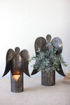 Decorative angel-shaped candle holders with a plant on a light surface.