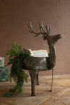 Decorative metal reindeer with greenery on a wooden surface against a brown wall.