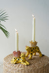 Two leopard-shaped candle holders with candles on a woven surface.