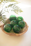 Green glass spheres in a wooden bowl with ferns in the background