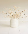White vase with dried flowers on a light wooden floor