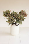 Faux green plant in a white vase on a light wooden floor.