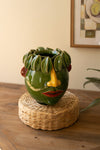 Green ceramic face vase on a woven stand with a neutral background