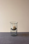 Clear glass candle holder with a lit candle on a gray surface and beige background