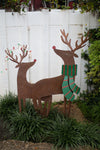 Decorative metal reindeer with a green scarf in front of a white fence.