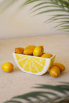 White ceramic bowl shaped like a lemon slice with lemons on a light surface