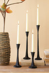Set of black candle holders with lit candles on a wooden surface, next to a woven vase and books.