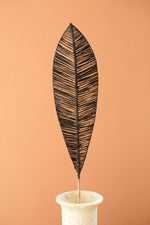 Decorative leaf sculpture on a stand against a peach background