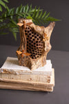 Wooden bee hive sculpture on a stack of books with green leaves in the background