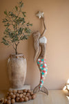Decorative mermaid figure with a star and a vase with greenery on a beige wall.