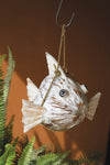 Decorative fish-shaped birdhouse hanging against a brown background with greenery.