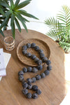 Decorative necklace on a wooden table with plants in the background