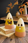 Two terracotta candy corn-shaped candle holders on a wooden surface with books and a vase in the background.