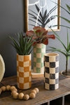 Decorative vases with plants on a wooden surface against a gray wall.