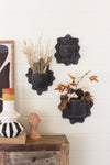 Decorative wall pieces with plants and a wooden cabinet against a white wall.