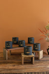 Set of blue candle holders with jack-o'-lantern faces on a wooden stand against an orange wall.