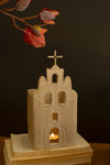 Small ceramic church model with a candle inside, placed on a stack of books against a dark background.