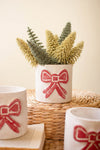 Decorative plant pots with red bow design on a woven surface