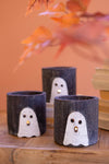 Three dark cylindrical candles with ghost designs on a wooden surface.