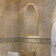 Bathroom with beige tiled walls, a decorative mirror, and towels.