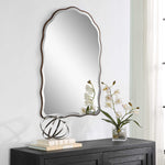 Decorative mirror on a wall above a dark wooden console table with books and a small plant.