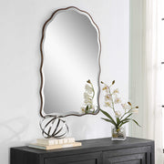 Decorative mirror on a wall above a dark wooden console table with books and a small plant.