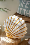 Shell-shaped decorative pillow with gold accents on a woven surface.