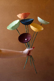 Hand holding a bouquet of colorful paper flowers against a brown background