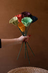 Hand holding a bouquet of colorful artificial flowers against a brown background