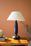 Table lamp with a black base and white shade on a wooden surface against an orange wall.