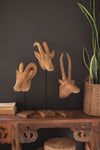 Wooden animal head sculptures on a wooden table against a dark wall with a plant in the background.