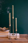 Set of tall, thin candles on a wooden surface with a dark green background