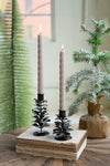 Two lit candles in decorative candle holders on a book with a Christmas tree and gift bag in the background.