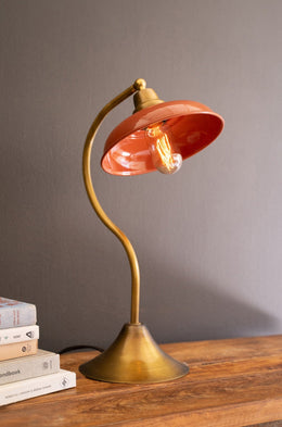 Table lamp with a red shade and brass base on a wooden surface.