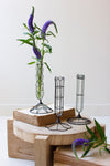 Decorative wire candle holders on a wooden stool with a vase of purple flowers.