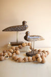 Decorative wooden birds on stands with a ring of wooden beads on a neutral background