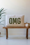 Pillow with 'OMG' text on a wooden bench against a white wall