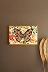 Framed artwork of a butterfly with floral patterns on a brown wall.