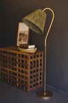 Floor lamp with a green lampshade next to a wooden side table against a dark wall.