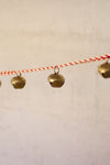 String of brass bells with red and white string on a beige background