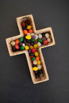 Wooden cross-shaped container filled with colorful jelly beans on a dark background