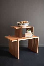 Wooden side table with a bowl of fruit and books against a gray wall.