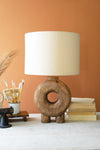 Wooden table lamp with a white shade on a surface against an orange wall.